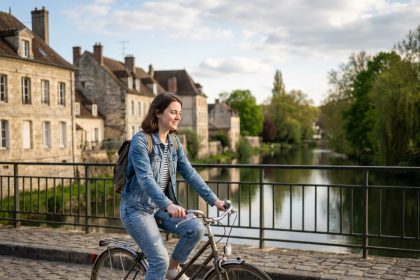 Jeune femme à vélo sur un pont à Compiègne avec rivière et bâtiments